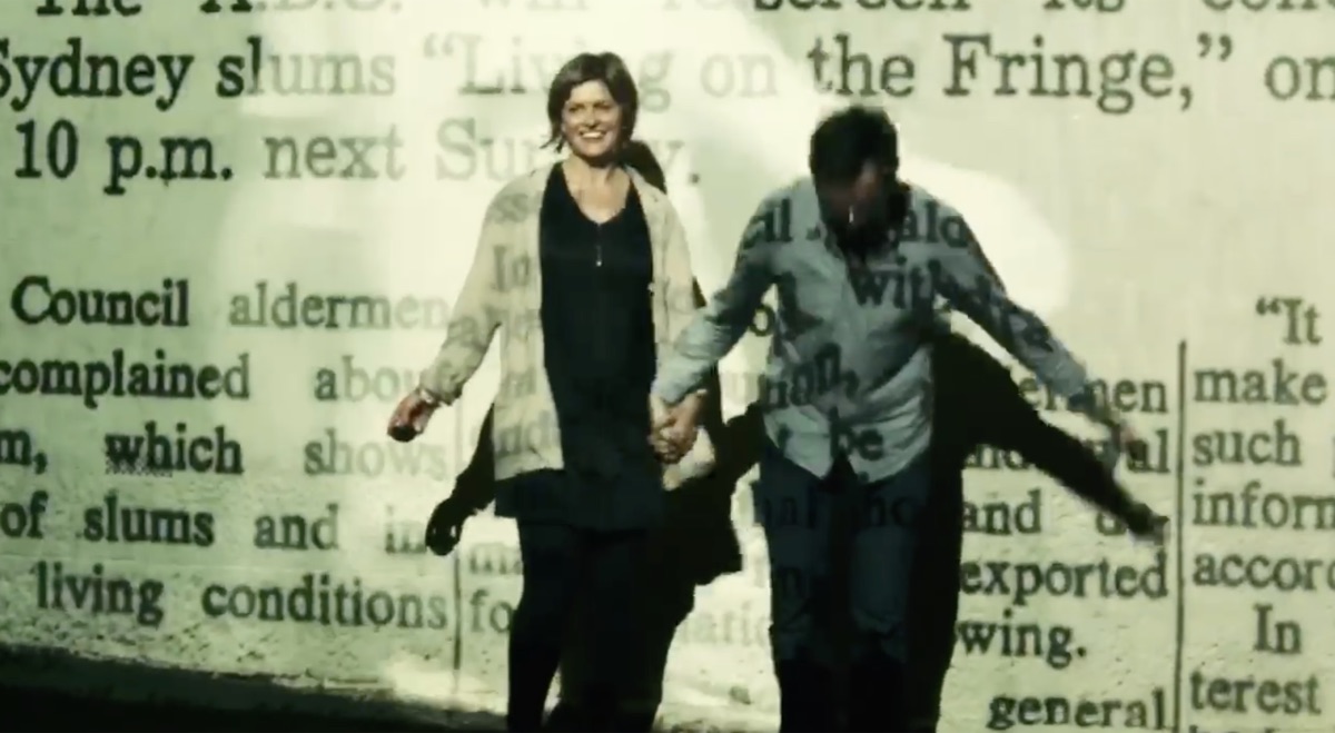 Couple walking through projected archival newspaper text about Sydney's inner-city housing